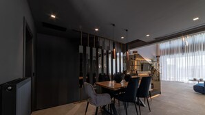 A modern dining area with a wooden table and chairs, a decorative wall, and a large window with sheer curtains. - Beautiful 4-Bed Villa Ria in Vathianos Kampos (Vathianos Kampos)