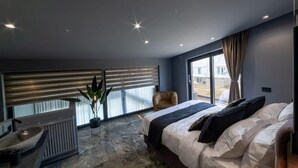 A modern bedroom with a large bed, a chair, a radiator, and a potted plant. - Beautiful 4-Bed Villa Ria in Vathianos Kampos (Vathianos Kampos)
