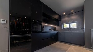 A modern kitchen with dark cabinetry, a built-in oven, and a window providing natural light. - Beautiful 4-Bed Villa Ria in Vathianos Kampos (Vathianos Kampos)