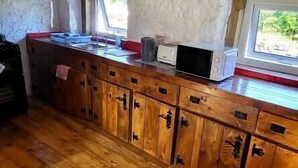 A rustic kitchen with wooden cabinets, a built-in microwave, and a window overlooking greenery. - Stunning 1-Bed Barn in Ballintubber (Ballintubber)