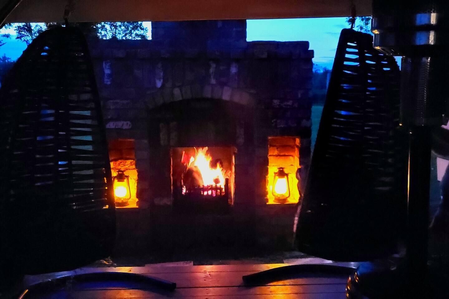 A stone fireplace with a fire burning inside, flanked by two lantern-style lights.