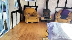 A cozy room with a wooden floor, a sofa, a bed, a TV, and a fireplace. - Stunning 1-Bed Barn in Ballintubber (Ballintubber)