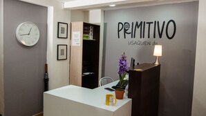 A reception desk with a clock, a sign reading "PRIMITIVO," and a potted plant. - Primitivo Usaquén dn (Bogotá)