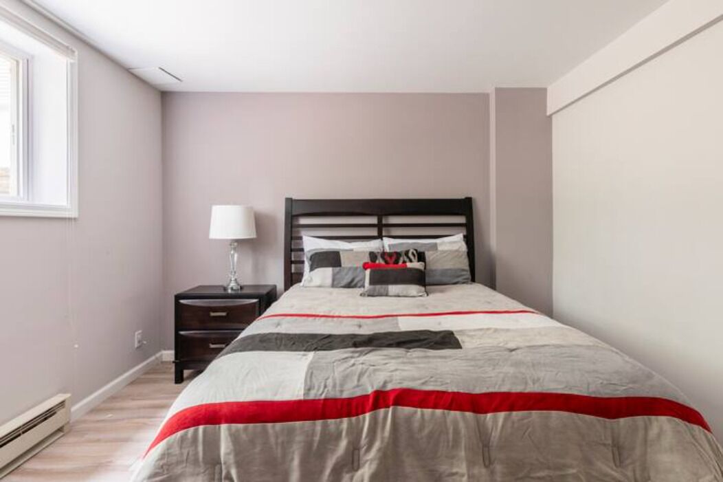 Un dormitorio con cama, mesita de noche, lámpara y ventana.