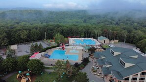 An aerial view of a resort with multiple swimming pools, a playground, and a building with a green roof.