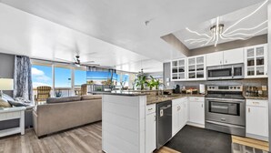 Een moderne keuken met witte kasten, roestvrijstalen apparatuur en uitzicht op het strand door grote ramen.