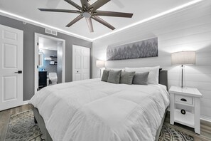 Ein Schlafzimmer mit einem großen Bett, einem Deckenventilator, einem Nachttisch mit Lampe und einem Bild an der Wand.