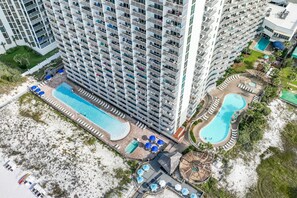 Ein Hochhaus mit mehreren Balkonen, einem großen Schwimmbecken sowie einem separaten Poolbereich mit Liegestühlen und Sonnenschirmen.