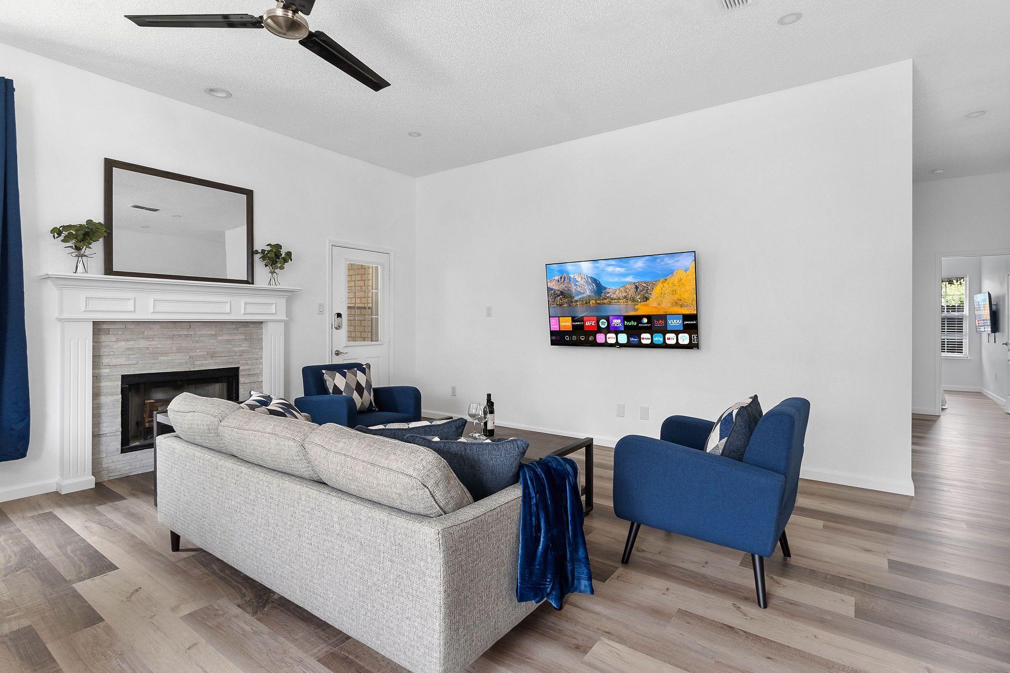 A modern living room with a fireplace, a mounted TV, and a ceiling fan.