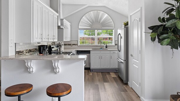 A modern kitchen with white cabinetry, a central island with stools, and a large window with a view of greenery. - Hidden Gem in Fort Worth with Hot Tub & Mini Golf (Watauga)