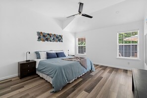 A bedroom with a bed, nightstand, ceiling fan, artwork, and windows. - Hidden Gem in Fort Worth with Hot Tub & Mini Golf (Watauga)