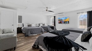 A modern hotel room with three beds, a ceiling fan, a TV, and a large window with curtains. - Hidden Gem in Fort Worth with Hot Tub & Mini Golf (Watauga)