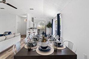 Enjoy meals in this stylish dining area with a long table set for a meal, featuring a sofa and kitchen in the background.