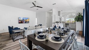 A modern kitchen with white cabinets, a dining area with a dark wooden table set for six, and a ceiling fan. - Hidden Gem in Fort Worth with Hot Tub & Mini Golf (Watauga)