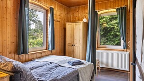 Une chambre dans une cabane en bois, avec un lit, une armoire, un radiateur et des rideaux.