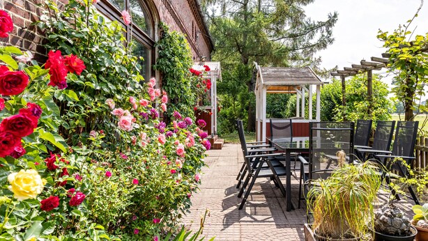 Un bâtiment en briques doté d’un espace jardin agrémenté d’une pergola, de sièges extérieurs et de plantes en pot.