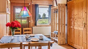 Un intérieur en bois avec une table à manger dressée pour deux personnes, une fenêtre avec des rideaux et une porte dotée d’une poignée.