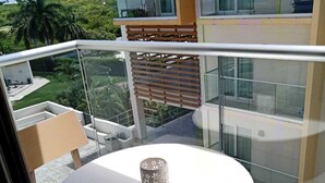Un balcon avec une table ronde et deux chaises, un vase décoratif, et une vue sur un paysage verdoyant et d’autres bâtiments.
