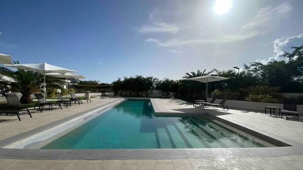 Une piscine rectangulaire à l’eau d’un bleu cristallin, entourée d’une terrasse carrelée et de chaises longues.