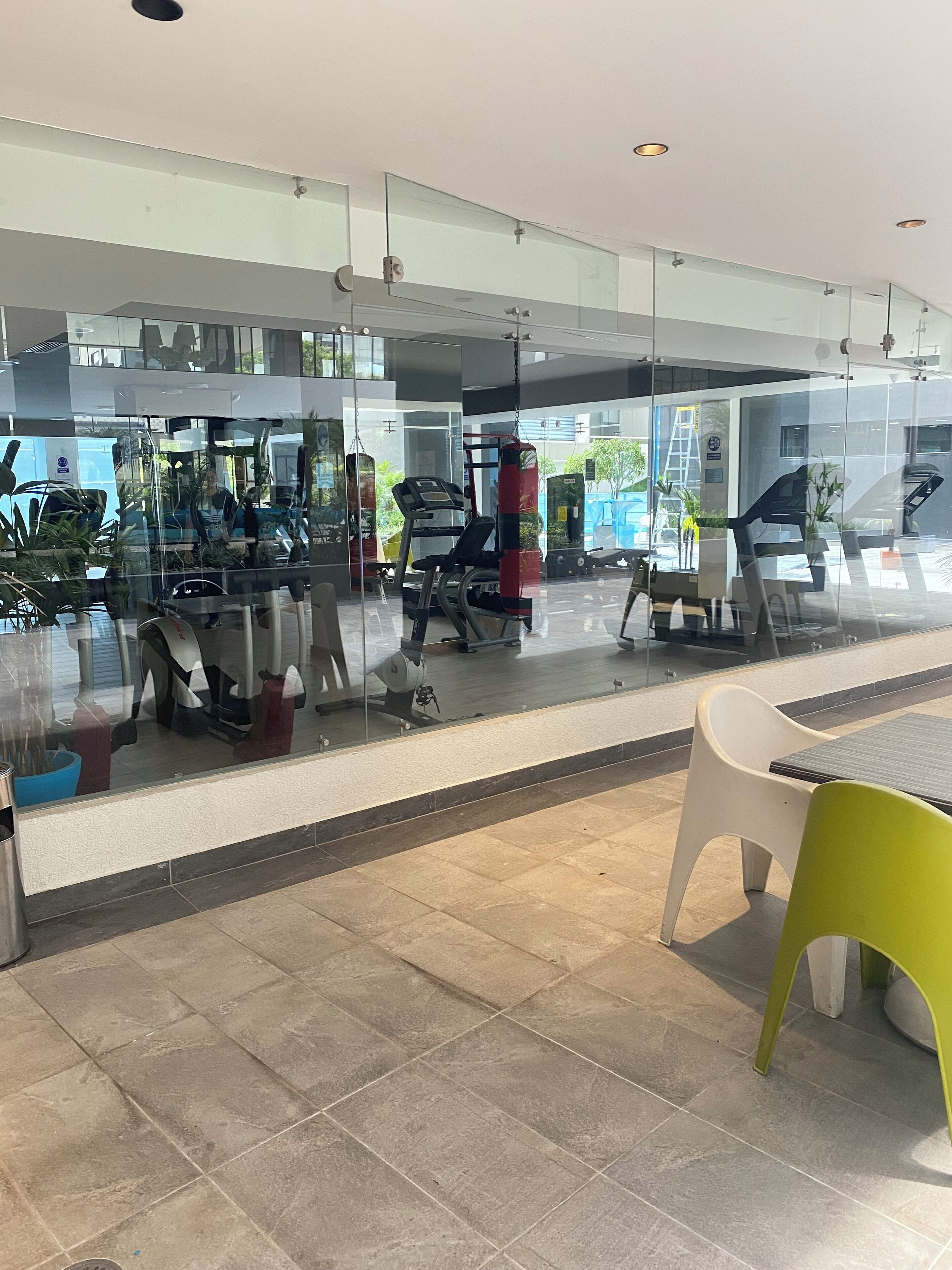 Una palestra moderna con attrezzi da ginnastica, pareti in vetro e un’area relax con sedie e tavoli.