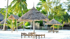 A beach with thatched umbrellas, wooden benches, and palm trees. - Coral Bay Zanzibar (Pongwe)