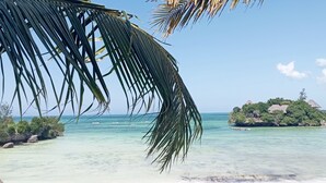 A tropical beach with clear turquoise water, a small island with a thatched-roof hut, and palm trees. - Coral Bay Zanzibar (Pongwe)