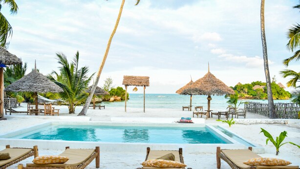 A poolside area with lounge chairs and thatched umbrellas, overlooking a beach. - Coral Bay Zanzibar (Pongwe)