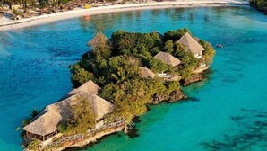 An aerial view of a tropical island resort with thatched-roof bungalows surrounded by clear turquoise waters. - Coral Bay Zanzibar (Pongwe)