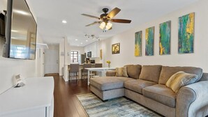 A modern living room with a sectional sofa, a dining table, and a kitchen in the background. - SoCo Condo, 2br/2ba, updated bright space with great pool + parking! (Austin)