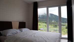 A hotel room with a large bed, a view of a mountainous landscape, and a balcony with a railing. - Lotus Villas (Mudrike)