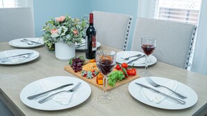 Een eettafel gedekt met borden, bestek, een wijnfles, een glas rode wijn en een fruitschaal.