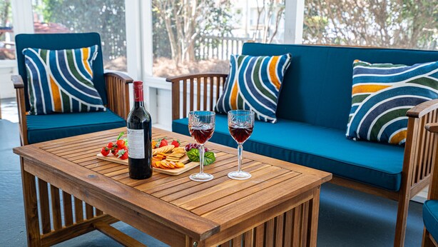 Een houten tafel met een fles wijn, twee glazen rode wijn en een schaal met lekkernijen.
