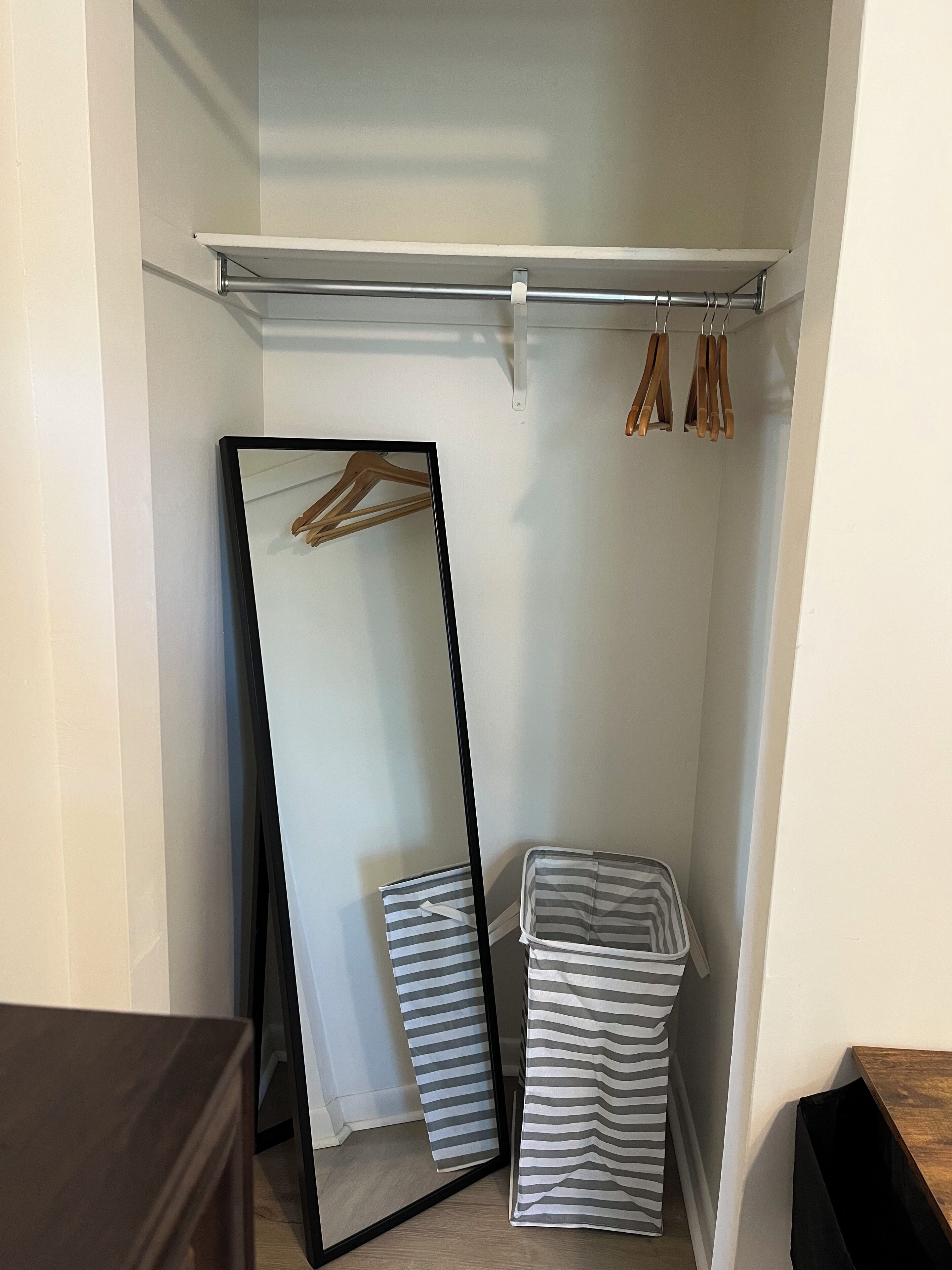A closet with a full-length mirror, wooden hangers, and striped storage bins.
