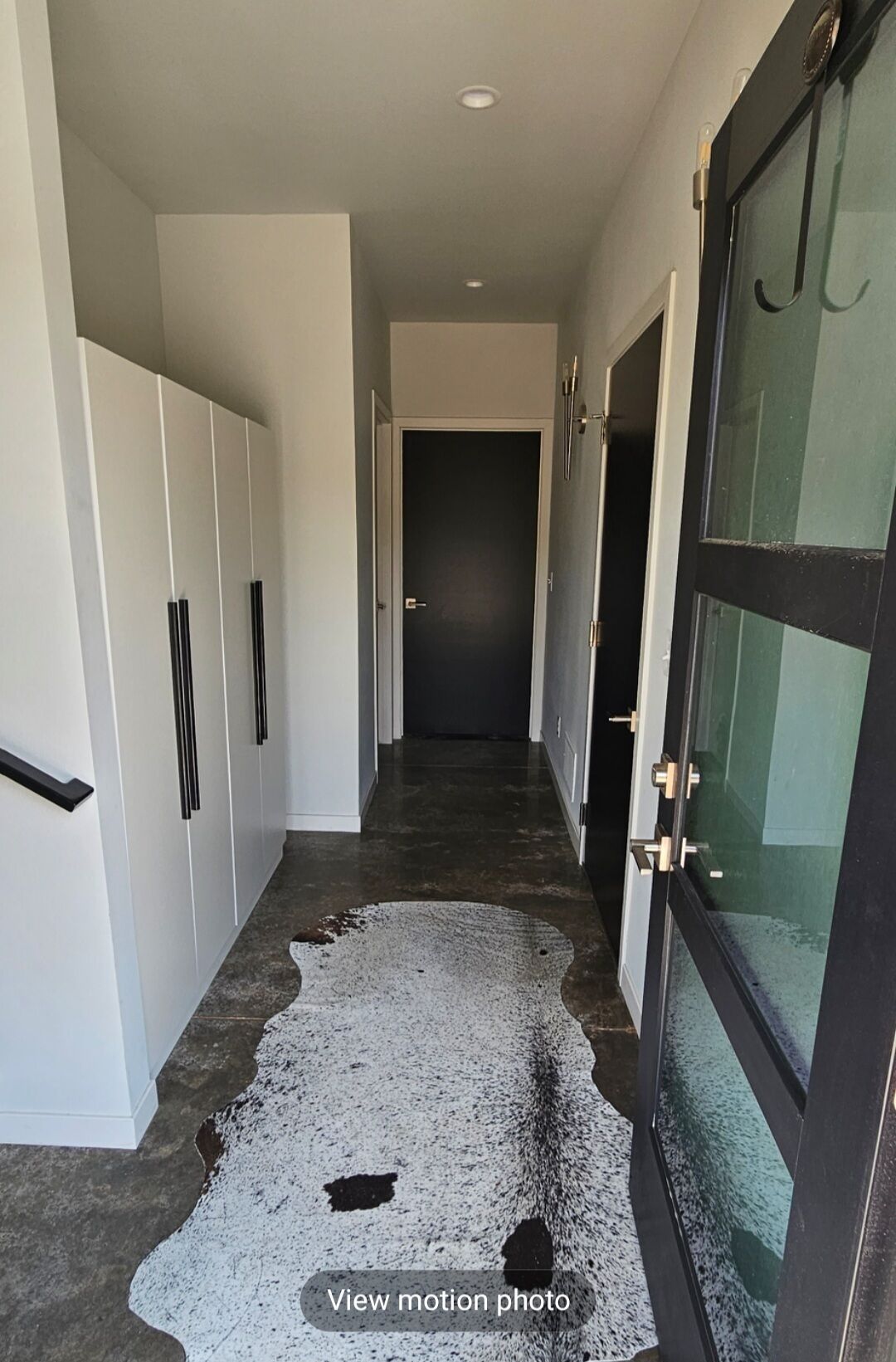Un couloir avec un plancher sombre, des murs blancs et une porte en verre sur le côté droit.