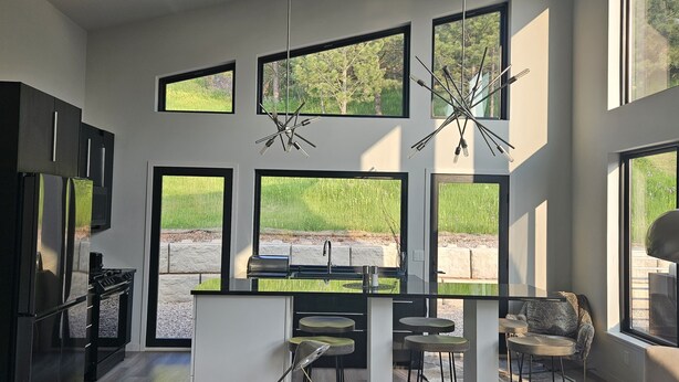 A modern kitchen with large windows, a central island, and a dining area with chairs.
