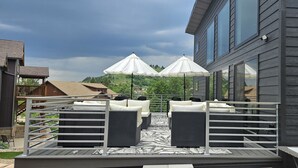 An outdoor deck with wicker furniture and umbrellas, overlooking a hilly landscape.
