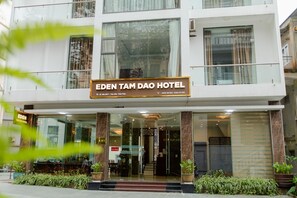 Exterior del Hotel Eden Tam Dao, con una entrada despejada, un cartel y un frente de vidrio.