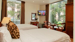 A hotel room with two beds, a TV, a desk with a chair, a lamp, and large windows with curtains. - Eden Tam Dao Hotel (Tam Dao)