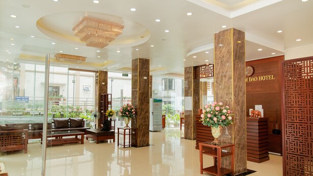 A hotel lobby with marble columns, wooden reception desk, and a large chandelier. - Eden Tam Dao Hotel (Tam Dao)