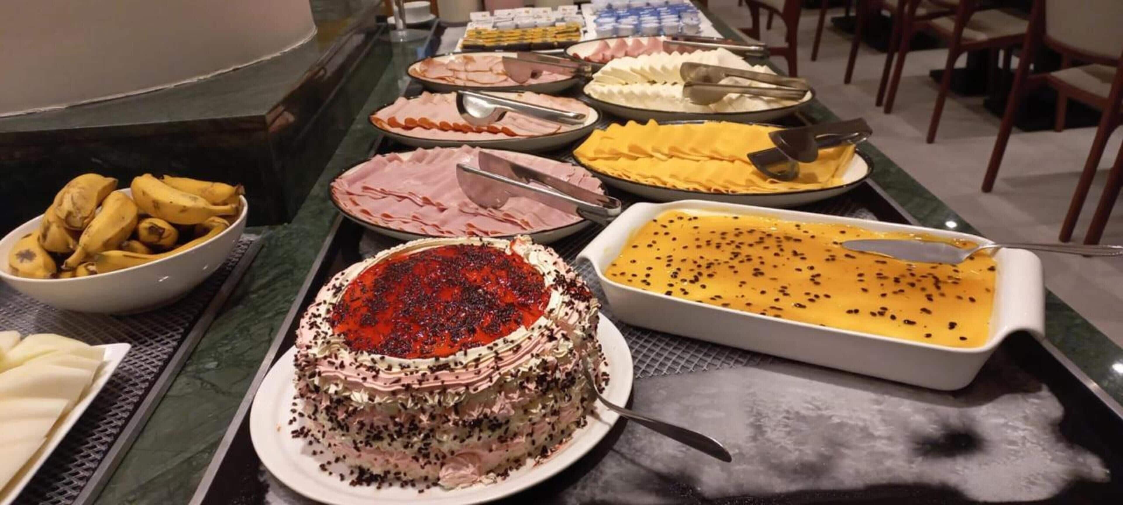 Un buffet proposant divers plats, notamment un gâteau recouvert d’un glaçage rouge, un plat jaune parsemé de graines noires et un saladier de bananes.