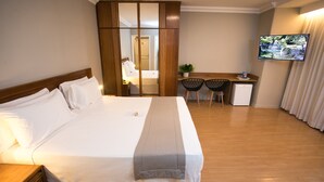 Una habitación de hotel con una cama grande, un escritorio, dos sillas, un refrigerador pequeño y un televisor en la pared.