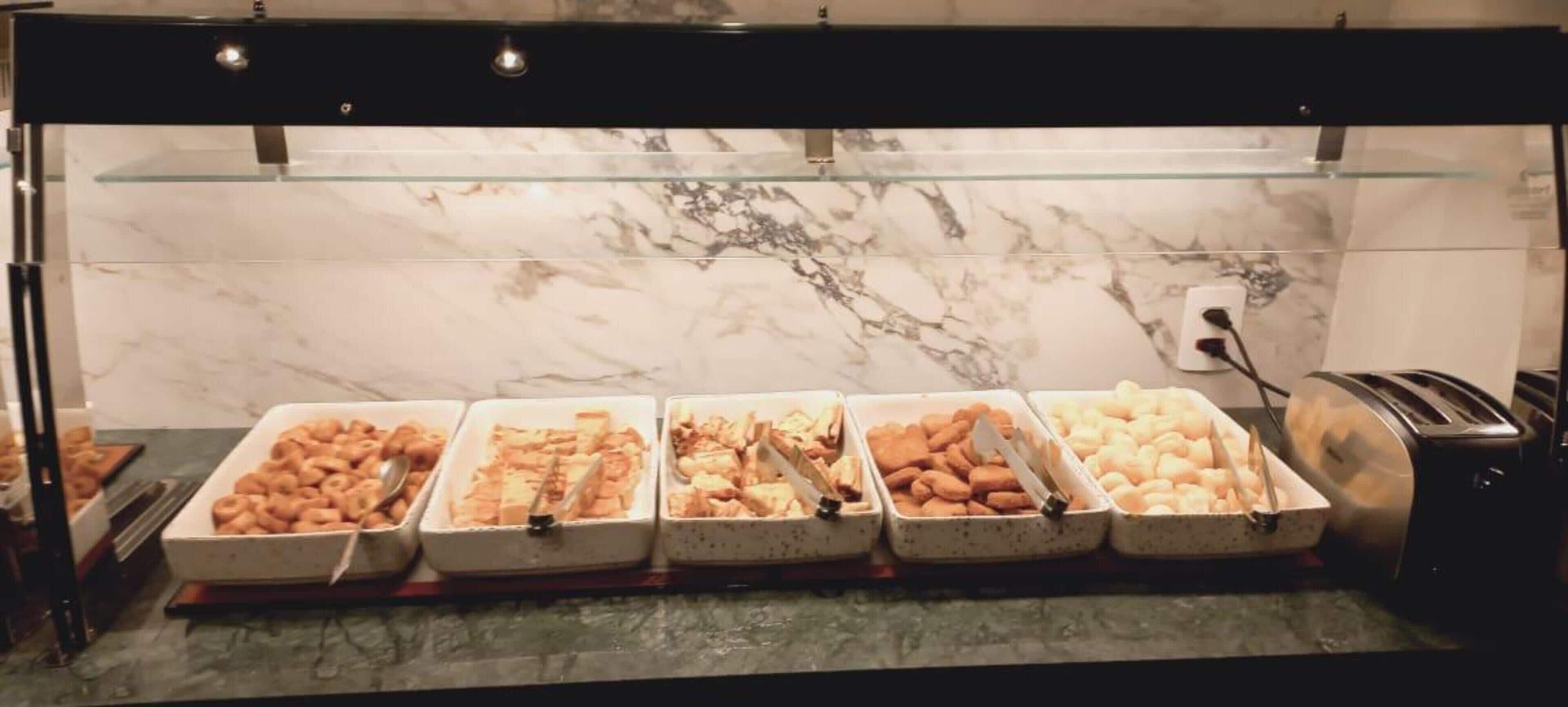A buffet with various food items, including pastries and bread, displayed in white trays.