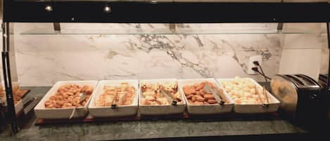 A buffet with various food items, including pastries and bread, displayed in white trays.