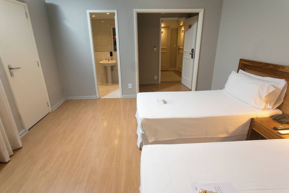 A hotel room with two beds, a wooden floor, and a bathroom visible through an open door.