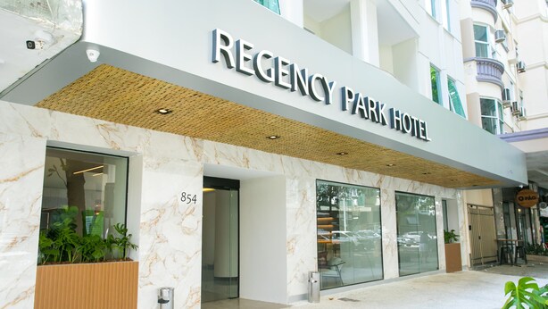 Exterior del hotel Regency Park, con fachada moderna, amplias ventanas de vidrio y una entrada destacada.