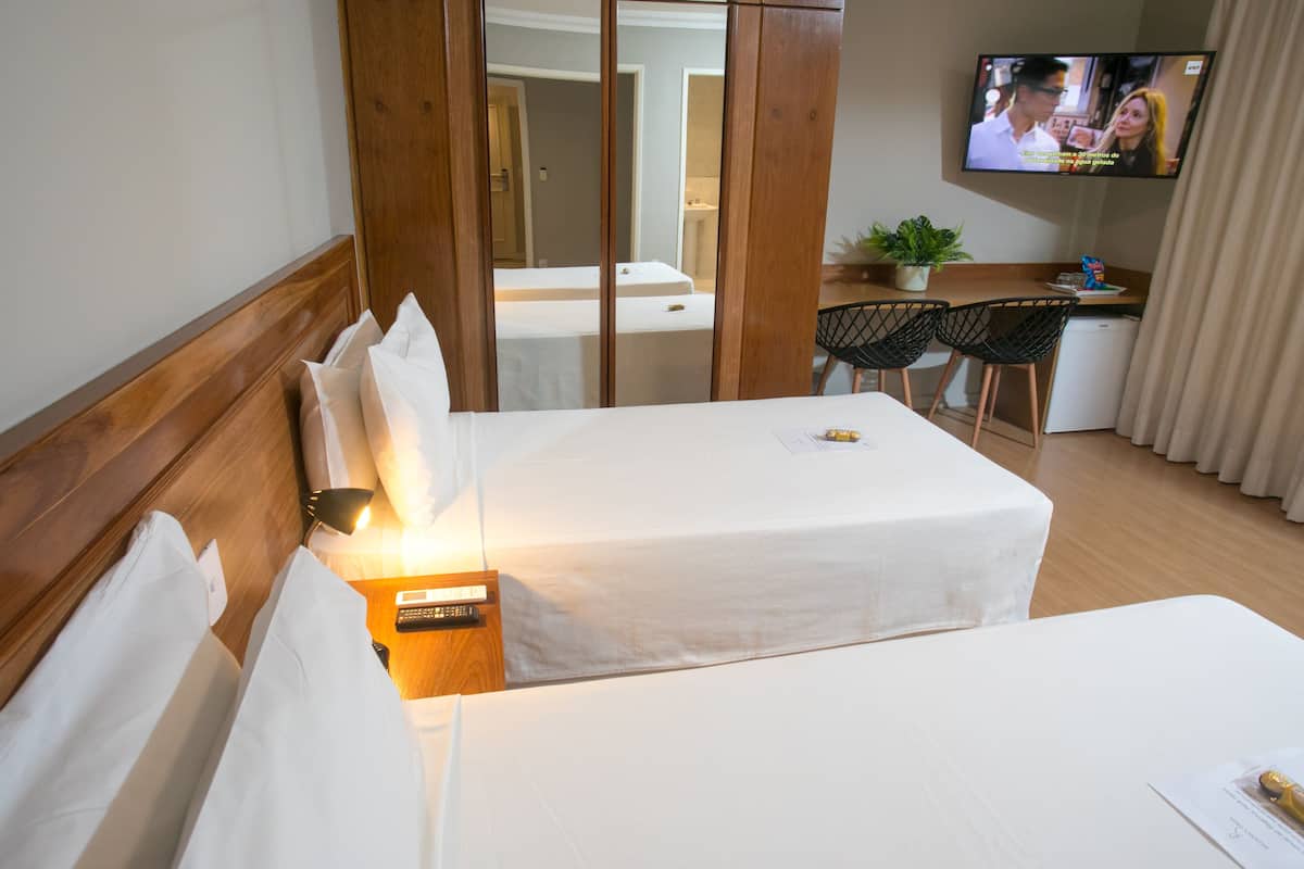 A hotel room with two beds, a desk with a chair, a TV, and a small kitchenette area.