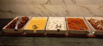Un bufé con distintos alimentos, incluyendo carne, queso, huevos y un plato a base de tomate.