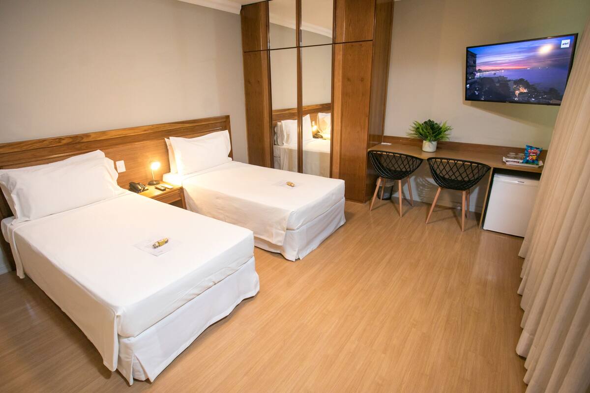 A hotel room with two beds, a desk with a chair, a television, and a small kitchenette.