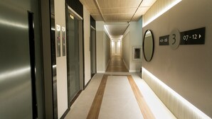 Un pasillo moderno de hotel con ascensores, un corredor que lleva a las habitaciones y un letrero en la pared que indica la habitación número 3 con las fechas 07-12.
