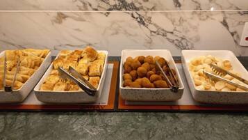 Fyra brickor med olika matvaror står på en bänkskiva av marmor, och bredvid dem ligger ett par serveringstänger.